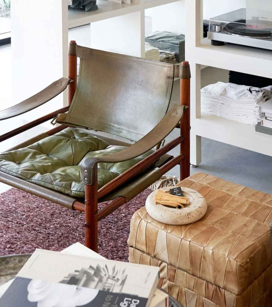 Green leather and wood lounge char nex tto a leather stool with a round dish.