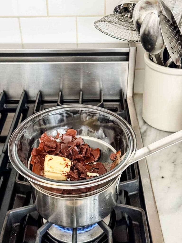 Melting chocolate and butter on stovetop in glass bowl over pan of water. 