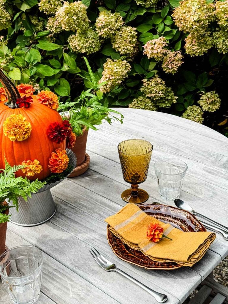 A tablescape with polka-dot pumpkins on galvanized cake stands, plants in terracotta pots, plate with gold napkin.