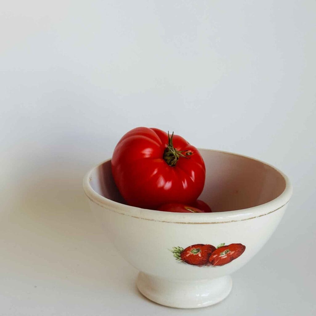 Small bowl with a tomato on the side and an heirloom tomato in the bowl.