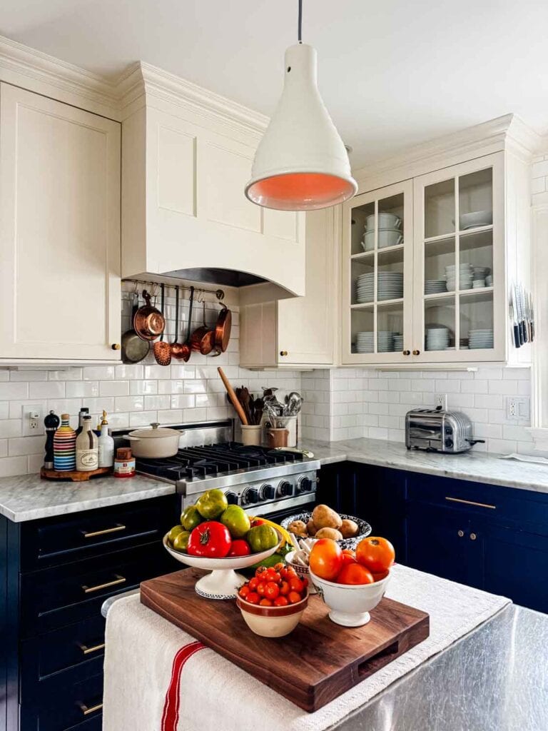 Vintage bowls filled with tomatoes on a wood cutitng board on a grain sack on a kitchen island.