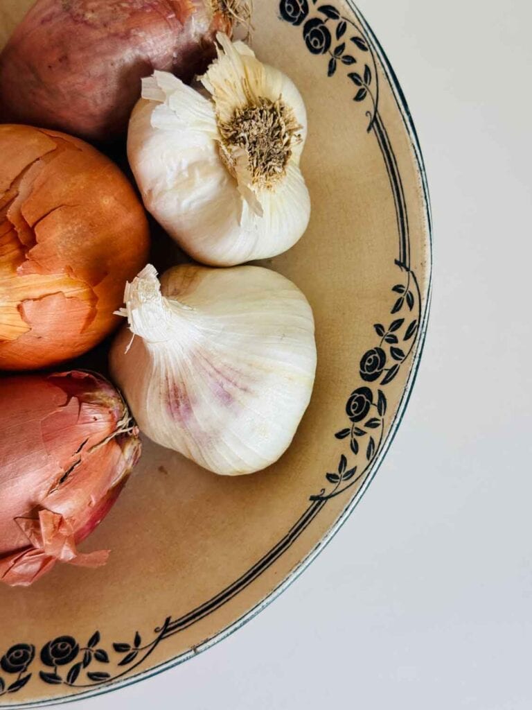Vitnage bowl with blue flower trim holding garlic, and shallots. 
