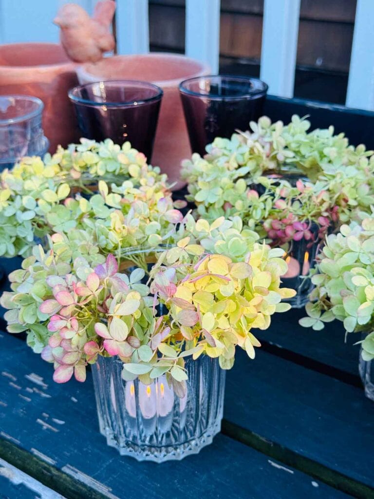 Votive candles burning in glasses with Hydrangea leaves as a crown.