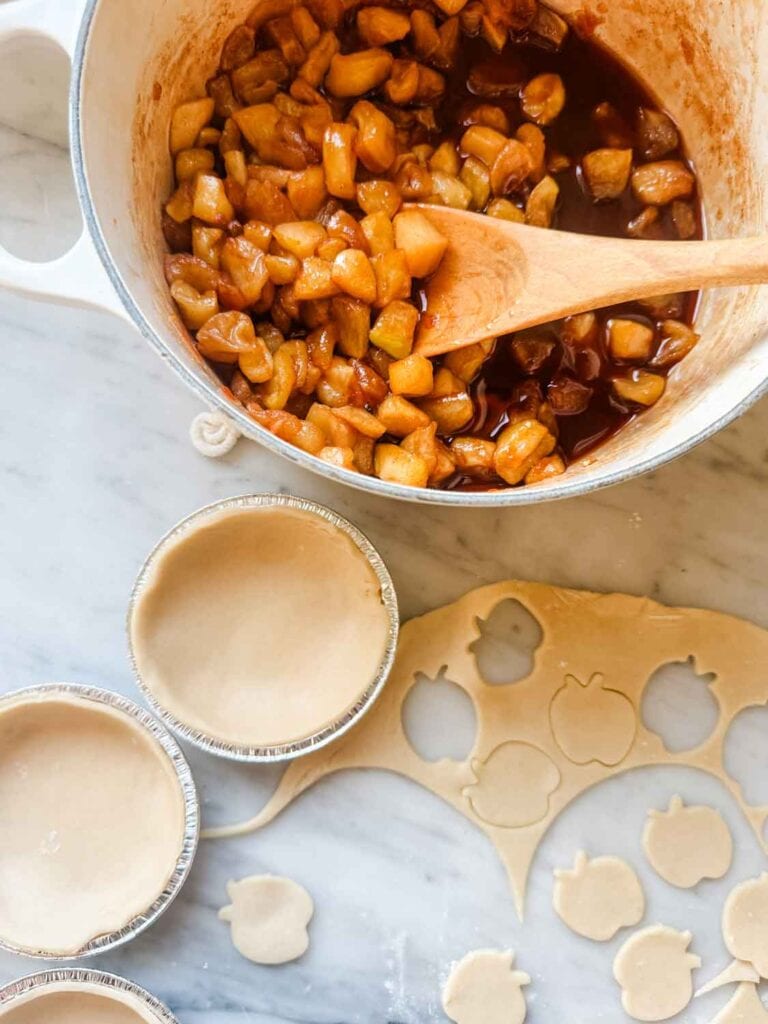 Cooked apples in Le Creuset with mini apple pie tins with bottom crust and cut out mini apple pastry. 