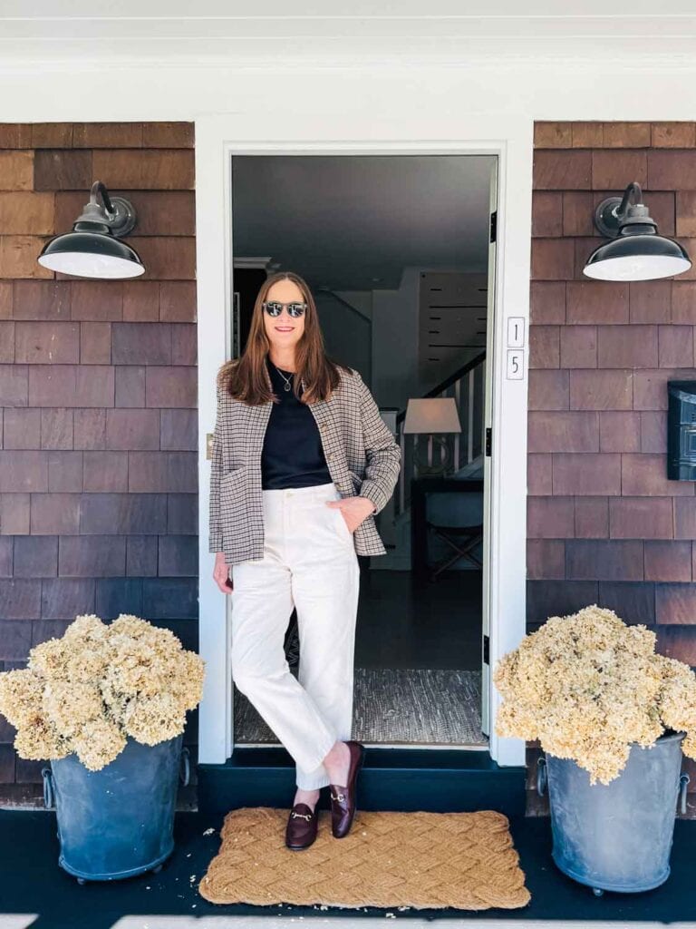 Annie Diamond weraing the Sézane Will houndstooth jacket with A;ex Mill Neil pants in ecru color, stanind in a cottage doorway.